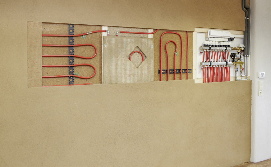 Diese funktionsfähige Musterfläche einer Wandheizung in Nass- und Trockenbauweise mit sämtlichen Komponenten, einschließlich der Wärmeverteilschicht aus Lehmputz, befindet sich in der Ausstellung eines Handwerkbetriebs.