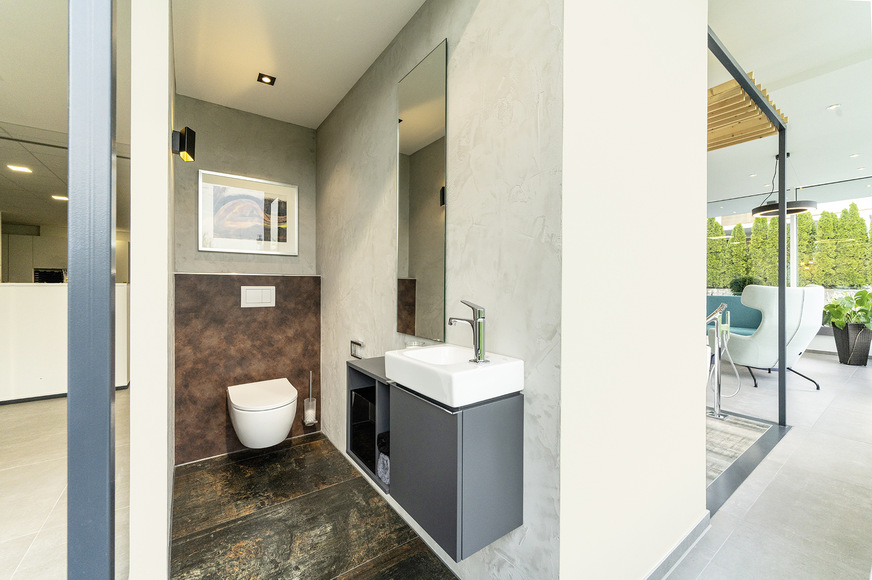 Im hinteren Bereich von Cube 1 ist ein renoviertes Gäste-WC dargestellt: die in vielen Altbauten noch typische WC-Anlage mit bodenstehendem Klosett und wandhängendem Spülkasten wurde in eine saubere, aufgeräumte Unterputzlösung verwandelt. Die Innenwände der Cubes nutzen Kaltmaiers gezielt auch dazu, ihre Kunden hinsichtlich der Wandbeläge, inklusive besonderer Putz- und Spachteltechniken, zu beraten.