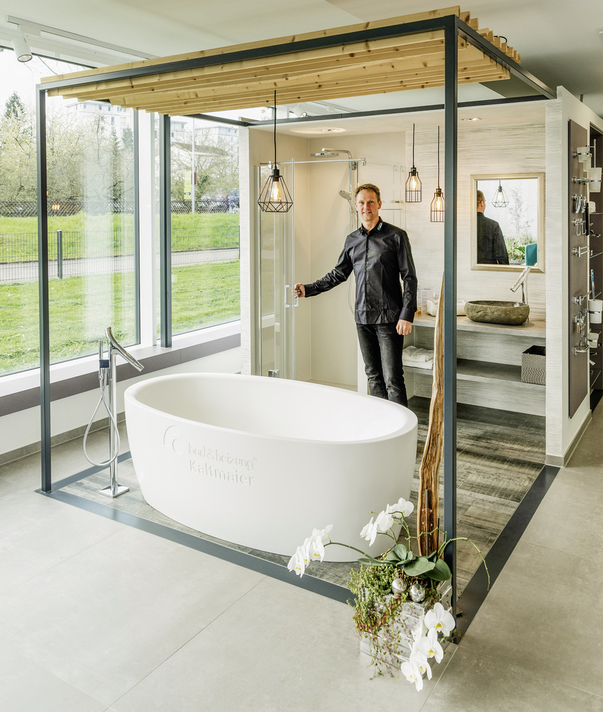 Das Bad mit „Loft“-Charakter im ersten Cube dient als Blickfang: frei stehende Badewanne mit Kaltmaier-Logo, Waschbecken in organischer Form, ­herabhängende Lampen. Praxis-Ausstattungsdetails: im Duschbereich eine Kabine mit Tür, die nach außen und innen aufgeht, sowie Großformatfliesen aus einem Stück (pro Wandbereich).