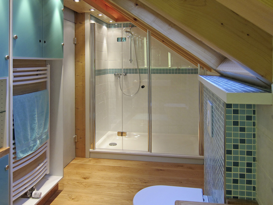 Im Duschbereich entschieden sich die Kunden für eine Duschtasse aus Stahlemaille. Die geschlossene Oberfläche verringert das Risiko, dass Wasser in die Holzkonstruktion eindringt. Die WC-Vorwand wurde mit einem Glasmosaik belegt.