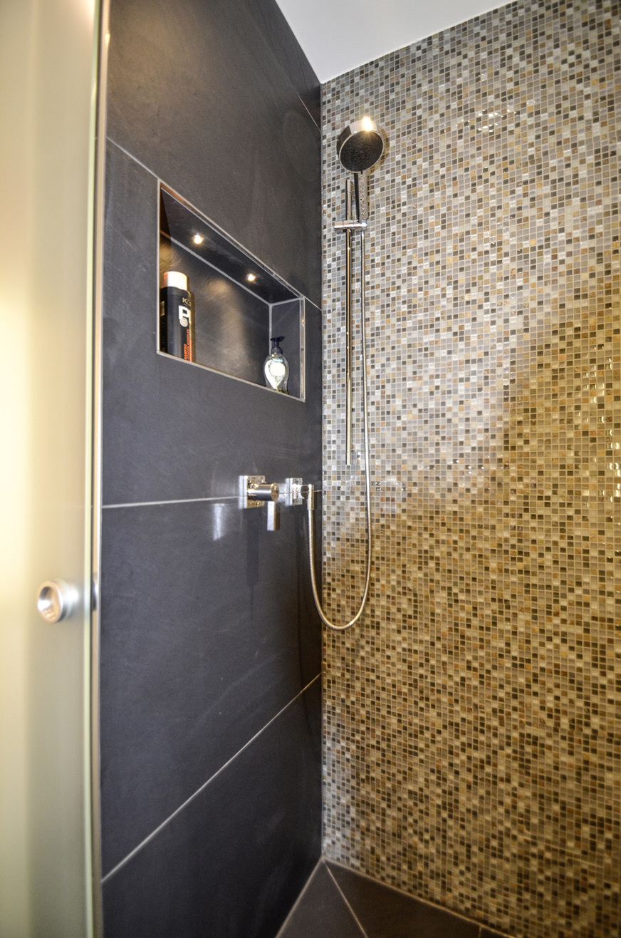 Mosaik mit Metalleinschlüssen schafft Tiefe an der Rückwand der Dusche und nimmt dem dunklen Schieferbelag die Strenge.
