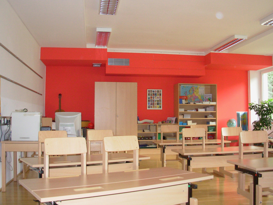 In diesem Klassenzimmer wurde das Schullüftungsgerät samt Anschlusskanal nicht sichtbar in einer Abkofferung ausgeführt. Im Fenstersturzbereich sitzt eine Wanddurchführung nach außen zum kombinierten Design-Fassadenelement mit Zu- und Fortluftöffnung.