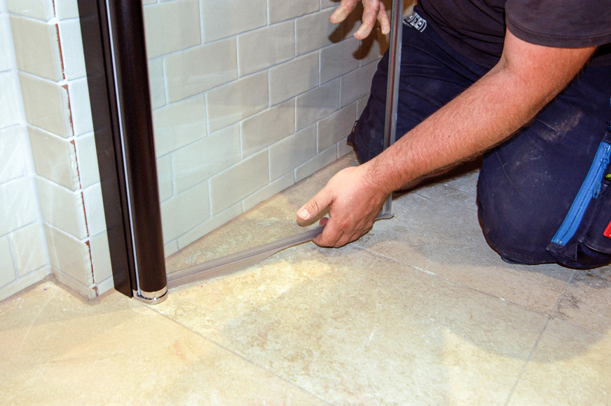 Einer der letzten Arbeitsschritte, ehe eine Duschabtrennung fertig montiert ist – die Schwallleiste wird angebracht.