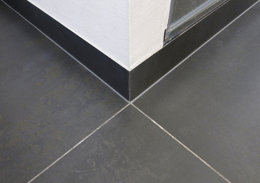 Die hohe Kunst der Verlegung zeigt sich an der Ecke der Dusche, wo alle Fugen exakt aufeinandertreffen. Die Sockelfliesen sind hier auf Gehrung geschnitten und flächenbündig eingeputzt.