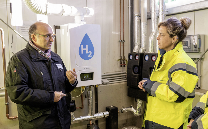 Remeha-Vertriebsleiter Franz Killinger und NRW-Wirtschaftsministerin Mona Neubaur im Gespräch vor dem 100-%-Wasserstoff-Brennwertkessel von Remeha.