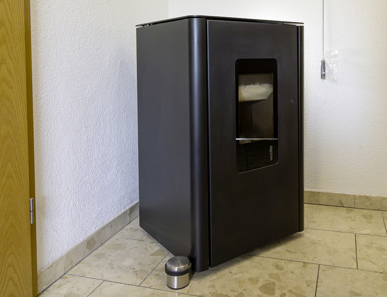 Der wasserführende Pelletofen, der im Flur des Eigenheims steht, ist an den integrierten Wärmespeicher der Wärmepumpen-Inneneinheit angeschlossen und liefert zusätzliche Heizenergie.