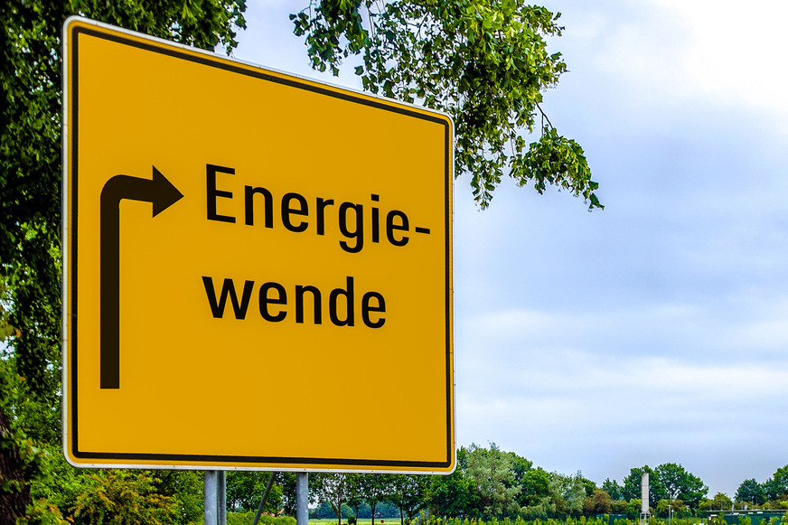 Wegweiser mit Aufschrift Energiewende zeigt auf Biogas-Anlage im Hintergrund