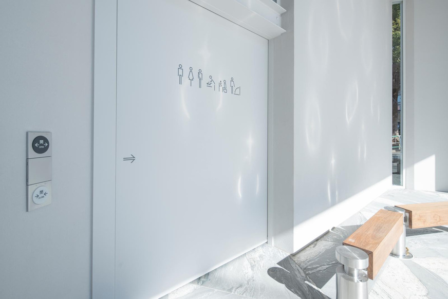 Piktogramme zeigen die vorhandene Ausstattung der jeweiligen Toilettenräume. Sie sind an der automatischen Schiebetür angebracht. 
