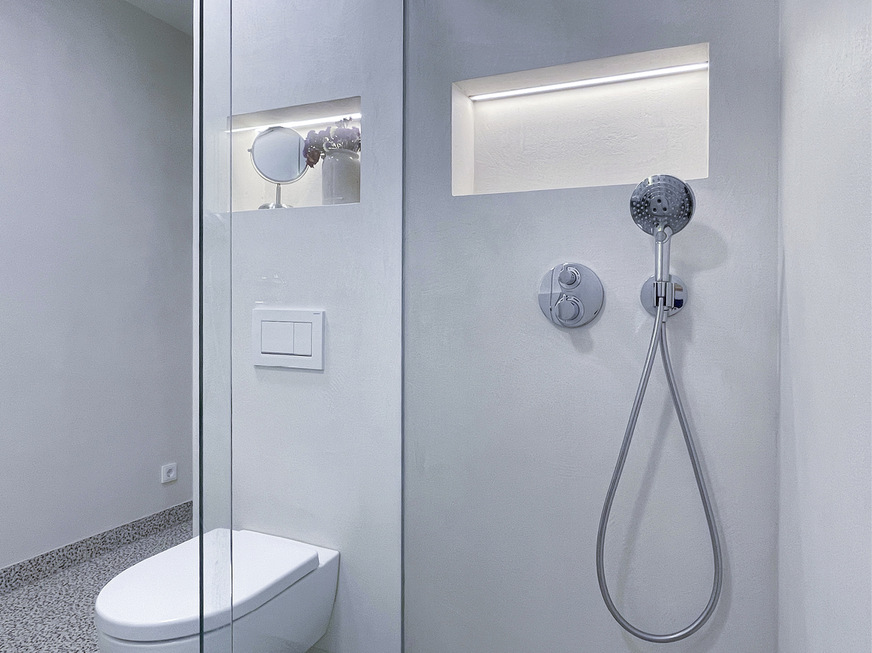 Zwei Nischen bieten Platz für Shampoo und Deko. Die Duschabtrennung besteht aus zwei Festglaselementen und einer Schiebetür.