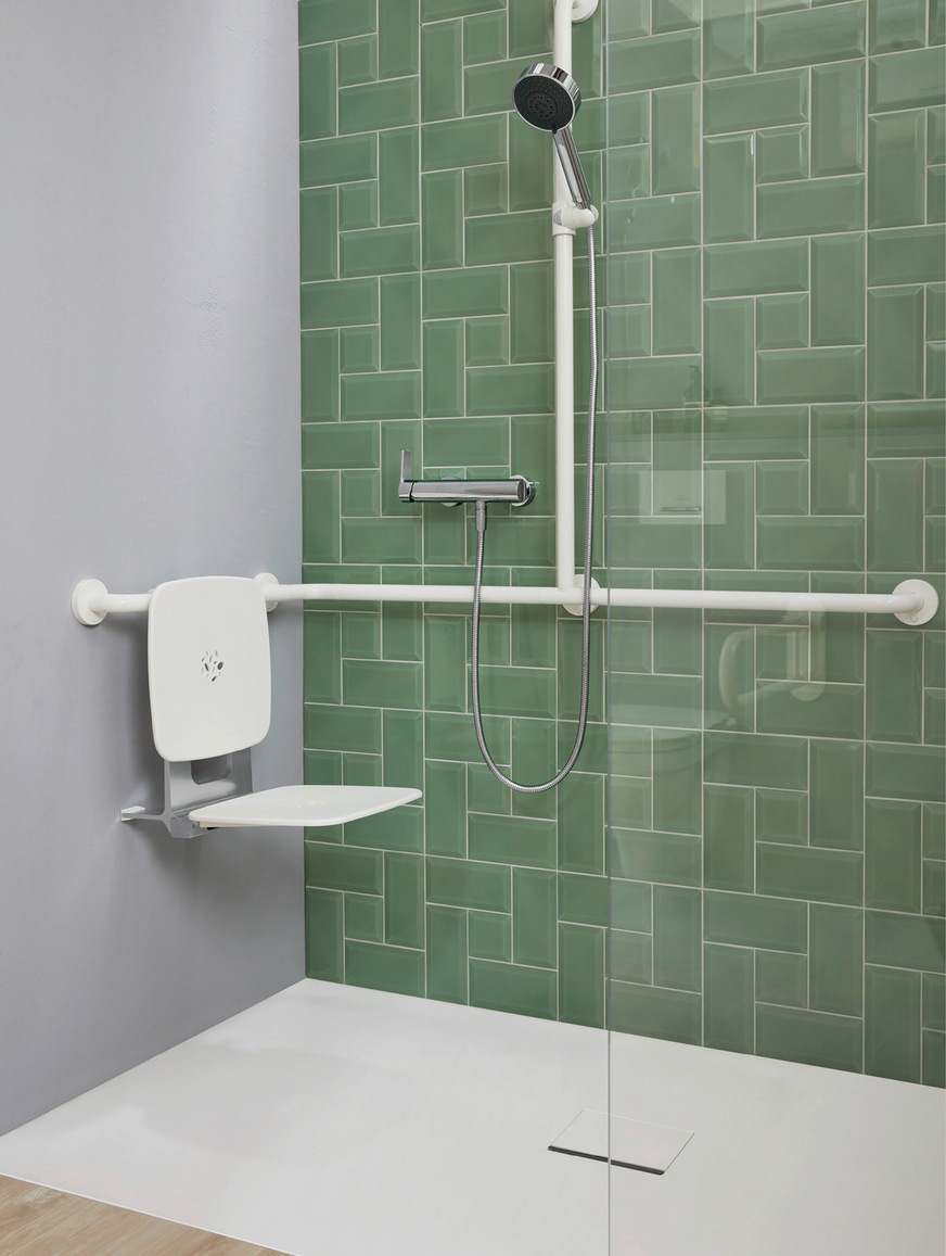 Die Kombination aus grüner Fliese in kreativem Verlege­raster mit hellem Holz wirkt freundlich, aber nicht unruhig. Durch Kontraste gut erkennbar: Duschsitz, Haltegriffe und Duschgestänge in Weiß statt Chrom.