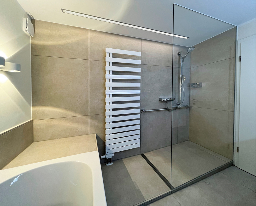 Das über die Rinne überlaufende Wasser wird durch eine durchsichtige Schwallschutzleiste am Rand des Duschpodestes aufgehalten.