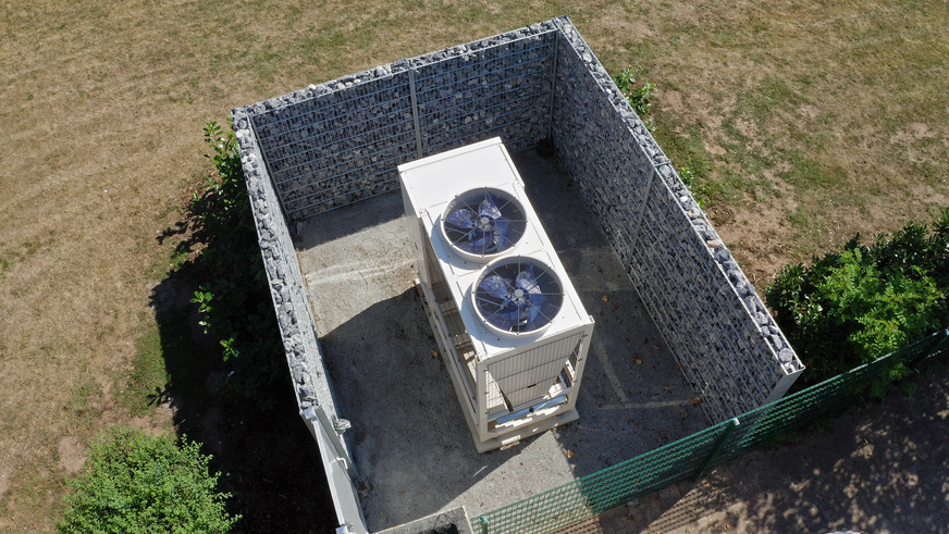 Aus Sichtschutzgründen von Gabionen umgeben, befindet sich die Luft-Wasser Wärmepumpe Aerotop®&nbsp;L65 von ELCO in der Grünanlage zwischen zwei der vier Häuser.