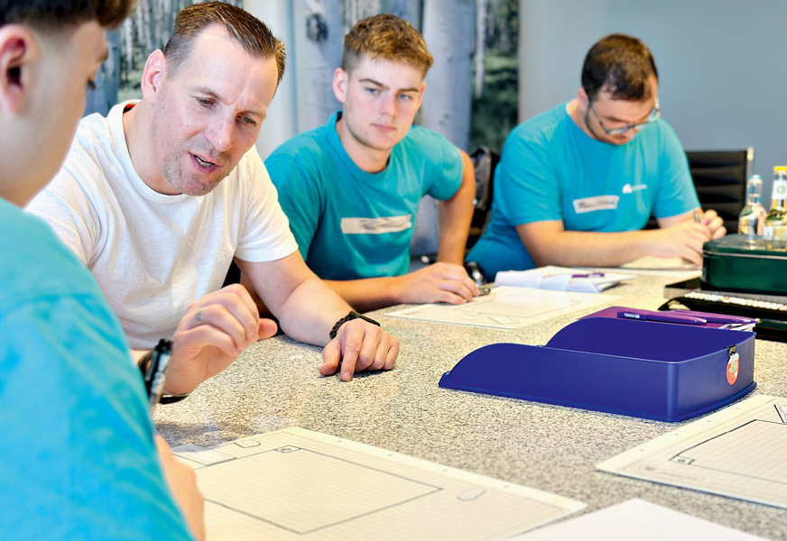 Der Leiter der Badsanierung plant mit den Auszubildenden ein Bad mit Badewanne, Dusche, Waschtisch und WC.