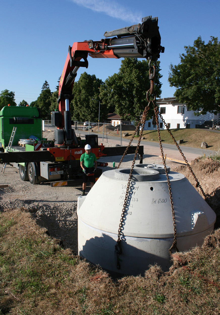 Versetzen des unterirdischen Pelletspeichers vom Lkw des Herstellers direkt in die vorbereitete Baugrube auf der Sportanlage „Im Haberfeld“ in Donaueschingen mit ca. 15 cm Sand und Feinkies als Auflagefläche.