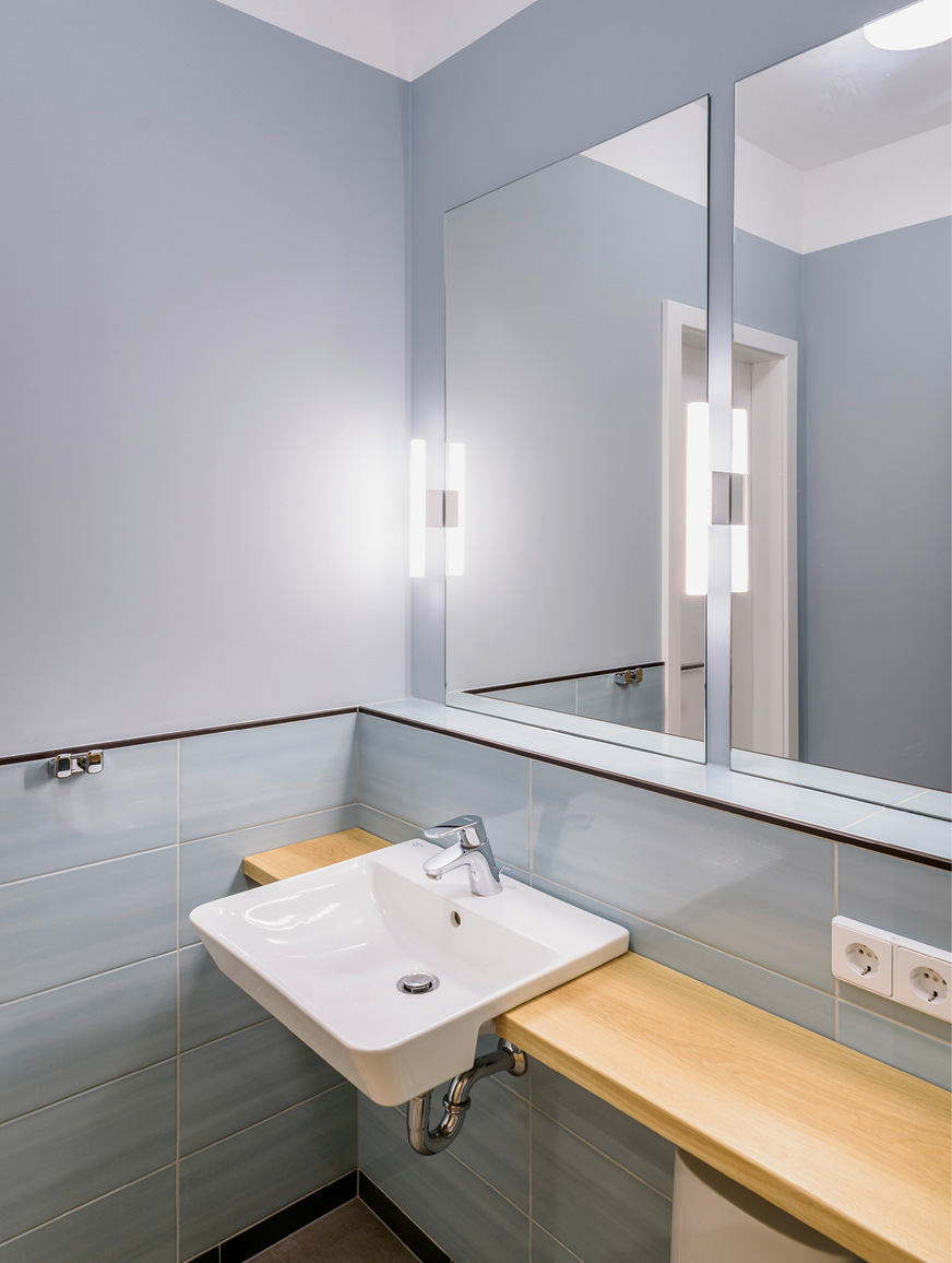 Dass Barrierefreiheit auch gut aussehen kann, zeigt das Mandanten-WC in einem Notariat. Der unterfahrbare Halbeinbau-Waschtisch wurde mit einer Echtholzplatte kombiniert, die sich als Ablage fortsetzt.