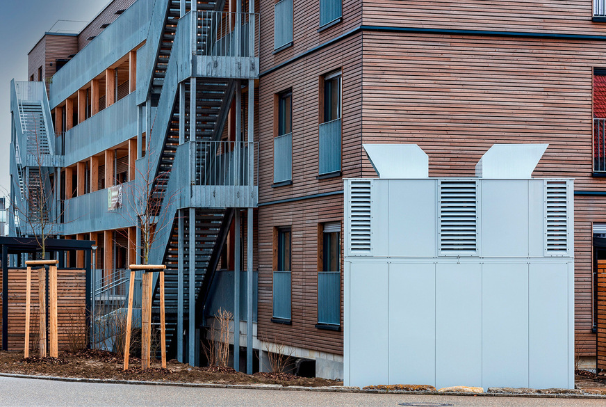 Die Luft/Wasser-Wärmepumpen stehen in einer Sicht- und Schallschutzeinhausung im Außenbereich an den Stirnseiten der Wohnblocks. Es werden jeweils zwei Wärmepumpen á 80 kW eingesetzt.