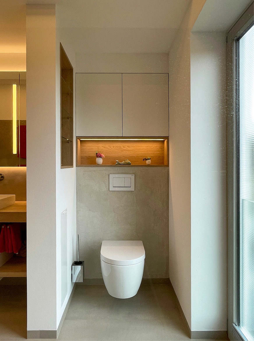 Im unteren Teil der Abtrennung ist ein Modul für Toilettenpapier und Reservepapier eingebaut. Die Vorwand über dem WC wird für einen Einbauschrank genutzt, eine beleuchtete Dekonische setzt einen weiteren Akzent.