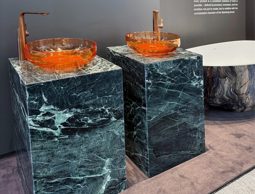 Das deutsche Unternehmen Steinberg inszenierte transparent-farbige Wannen und Aufsatzwaschtische aus Polyresin, kombiniert mit PVD-Armaturen auf Präsent﻿ations-Quadern aus grünlichem Verde-Alpi-Marmor. Großes Kino!