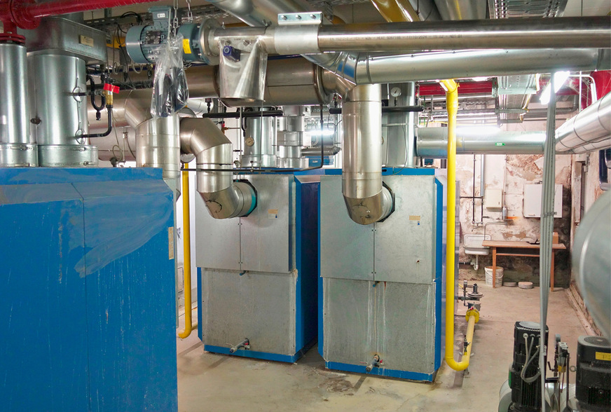 Die Wärmeversorgung der bisherigen Heizzentrale wurde monovalent über diese drei alten Gaskessel (2 x 1,15 MW, 1 x 1 MW) sowie ein Nahwärmenetz mit drei Strängen und 13 Unterstationen gewährleistet. Künftig soll die Grundlast mit einem Holzpellet­kessel (500 kW) abgedeckt werden. Zwei neue Gas-Brennwertkessel (2 x 1 MW) übernehmen die Spitzenlast.