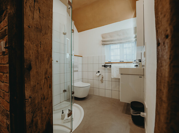 Die von der Inhaberin kultivierte „juckelige“ Patina aus altem Holz und Fachwerkmauern umrahmt das neu gestaltete Badezimmer mit modernen Badarmaturen und einem Toto WC – ein harmonisches Zusammenspiel von Alt und Neu.