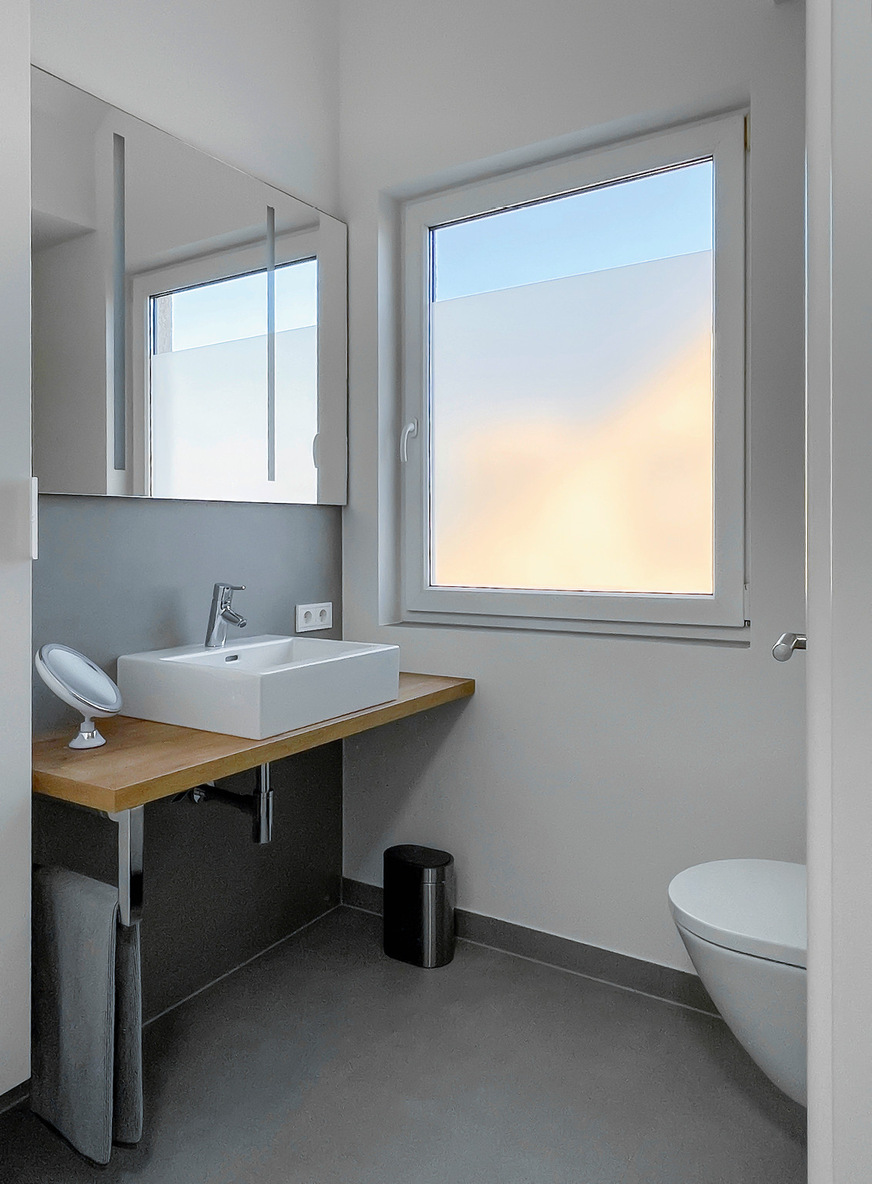 Der Waschtisch ist an der Wand zum Zimmer auf einer Ablageplatte in Holzoptik installiert.