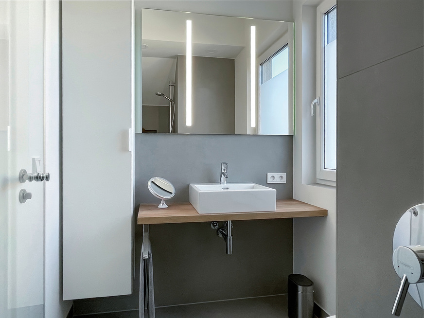 Ein durchgehender Spiegel mit integrierter Beleuchtung lässt den kleinen Raum größer wirken.