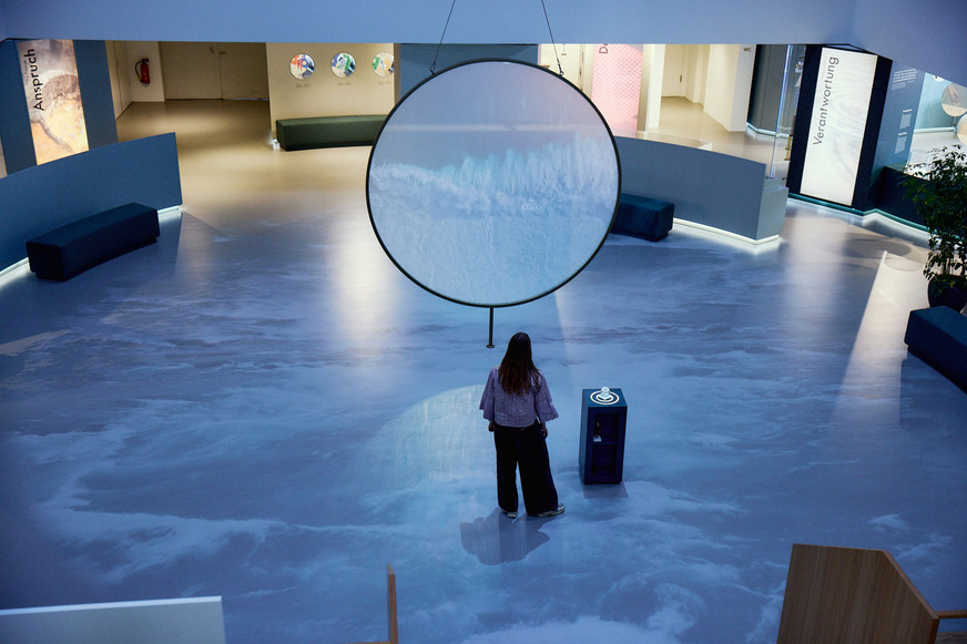 Der Rundgang durch die Ausstellung „Taktgeber des Wassers. Seit 1901.“ beginnt idealerweise im Zentrum der Ausstellung. Dort schwebt eine Acrylscheibe mit 3 m Durchmesser wie ein Wassertropfen im Raum.