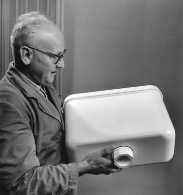 Ein Technischer Berater präsentiert einen der frühen Spülkastenmodelle aus PVC. Die Spülkästen komplett aus Kunststoff waren eine Weltneuheit in den 1950er-Jahren. - © Geberit
