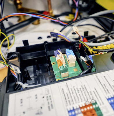  6 Im nächsten Arbeitsschritt werden folgende Komponenten miteinander verdrahtet: Spannungsversorgung, Buskommunikation sowie Außen- und Trinkwasserfühler. Zur Einrichtung der elektrischen Anschlüsse wird der Gehäusedeckel der Regelungseinheit am Kessel entfernt. Nachdem die Anschlussleiterplatte montiert wurde, kann der Endwiderstand in die Buchse an der Unterseite des Kit 65 gesteckt werden. Im Folgenden wird die Verbindungsleitung zwischen Kesselschaltfeld und Anschlussleiterplatte verlegt und der vorhandene 230-V-Anschlussstecker an die Netzanschlussleitung angesteckt. Auf der Unterseite des Gerätes wird die L-Bus-Leitung von Kit 65 in das Regelungsgehäuse des Gas-Brennwertkessels geführt und mit der innen liegenden Platine verbunden. Anschließend wird der Adapterstecker an der Erweiterungsleiterplatte SCB eingesteckt und die Vorrüstung für den Wärmepumpenanschluss und den Hybridbetrieb abgeschlossen. 