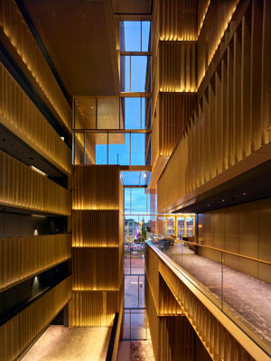 Das zentrale Atrium des Koenigshofs öffnet sich über mehrere Etagen hinweg zur Stadt und schafft eine visuelle Verbindung zwischen Innen und Außen. Warm hinterleuchtete Metallpaneele sorgen für eine elegante Lichtstimmung und verleihen dem Innenraum eine ruhige, fast sakrale Atmosphäre.