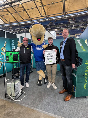 Gerne. Hier ist ein thematisch und zielgruppengerecht optimierter Alt-Text für das beschriebene Bild: Alt-Text: „Vier Männer, darunter ein Maskottchen im gebo-Kostüm, stehen am Messestand des Herstellers gebo vor Informationsmaterialien zu Rohrverbindungslösungen und innovativen Produkten für die SHK-Branche.“ Falls Details zum Kontext der Veranstaltung (z. B. Name der Messe) oder spezifische Produkte sichtbar sind, könnte der Text noch weiter angepasst werden – bitte geben Sie ggf. weitere Informationen an!. - © Zander / Fohrer