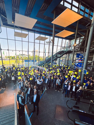 Gerne! Hier ist ein für die Zielgruppe und den Kontext optimierter Alt-Text: Alt-Text: „Fachbesucherinnen und -besucher der SHK-Branche auf einer Branchenmesse im modernen Foyer; viele Teilnehmende tauschen sich in kleinen Gruppen aus, einige halten gelbe Messe-Badges. Im Hintergrund führen Rolltreppen zu weiteren Ausstellungsbereichen.“ Begründung: Der neue Text verzichtet auf irrelevante Details (wie „bright lobby“) und beschreibt stattdessen präzise die Situation im Branchenkontext: Es handelt sich um Fachleute (Zielgruppe), es ist eine Branchenveranstaltung, und typische Interaktionen sowie Erkennungsmerkmale der Branche werden genannt. Damit dient er Nutzer*innen mit Assistenztechnik wesentlich besser als der generische Ausgangsvorschlag. - © Zander / Fohrer