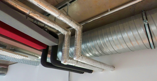 Deckengebundene Leitungen und farbige Schallschutzlamellen. Die Leitungen für Fußbodenheizung und Warmwasser sind gegen Wärmeverlust gedämmt, die Kaltwasser- und Regenwasserleitung gegen Wärmeaufnahme – letztere sind ­zusätzlich gegen Kondenswasserbildung diffusionsdicht ummantelt.