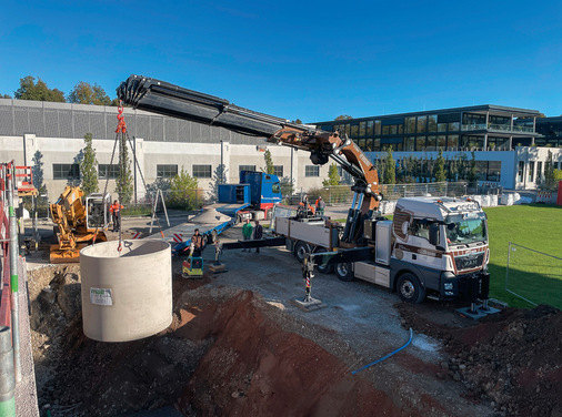 Versetzen der Regenspeicher vom Kran des Lieferfahrzeugs in die vorbereitete Baugrube. Fünf Betonbehälter, die untereinander verbunden sind, bilden die sogenannte Mehrbehälteranlage, der ein Filterschacht vorgeschaltet wurde. Dieser reinigt das vom Dach kommende Regenwasser.