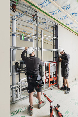 Montage der industriell vorgefertigten Installationstrennwand: Die beiden Handwerker richten das Modul aus.