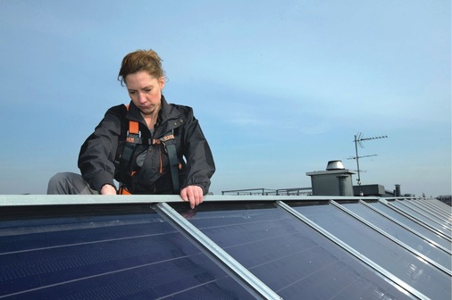 Eine Solarteurin installiert eine große Solaranlage für ein Mehrfamilienhaus auf den Dächern Berlins.