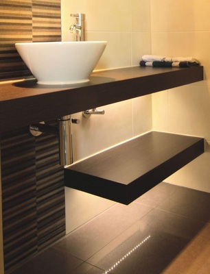 Die indirekte Beleuchtung in den Regal­böden spendet sanftes Licht und bringt den gewünschten Wow-Effekt. Die Waschtischplatte über die ganze Raumtiefe streckt den Raum.