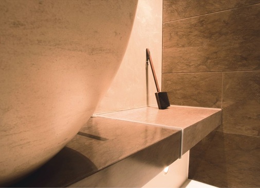 Die Natursteinkonsole, auf der die Wasch­schale thront, dient im Duschbereich als Bank.