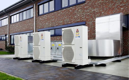 Das Lüftungsgerät, das im Hintergrund zu sehen ist, sowie die drei Wärmepumpen sind auf der Rückseite des Gebäudes aufgestellt.