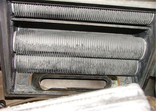 Das Foto zeigt die Wärmetauscherrohre eines Kessels bei schlechter Brennwertnutzung. Zwischen den Rohrrippen sind deutliche Ablagerungen zu erkennen.