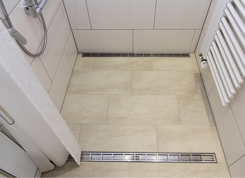 
Zwei Rinnen erhöhen die Ablaufkapazität und vermindern so stehendes Wasser undWasseraustritt in den Trockenbereich. Kleine Fliesenkanten als Wasserstop stellen oft eine Gefahr dar, da diese nicht unbedingt wahrgenommen werden.
