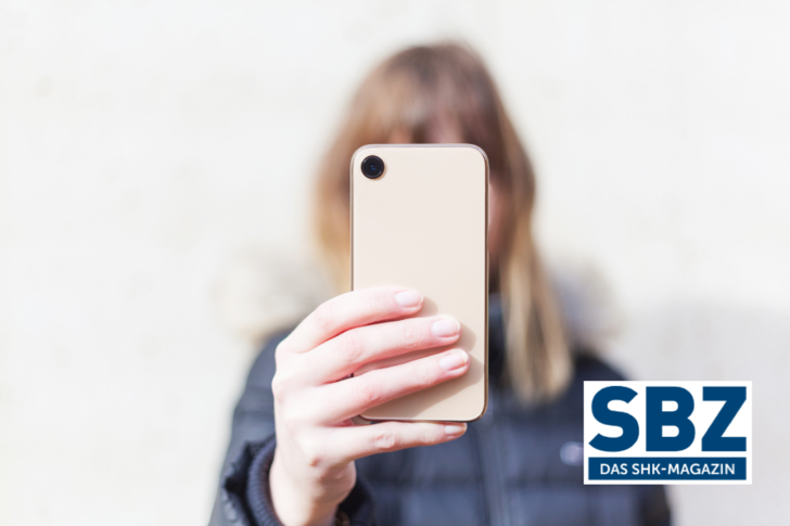 Person in dunkler Jacke hält sich ein Smartphone vor das Gesicht, in der Ecke das Logo der Zeitschrift SBZ. - © Adobe Stock / michelsass