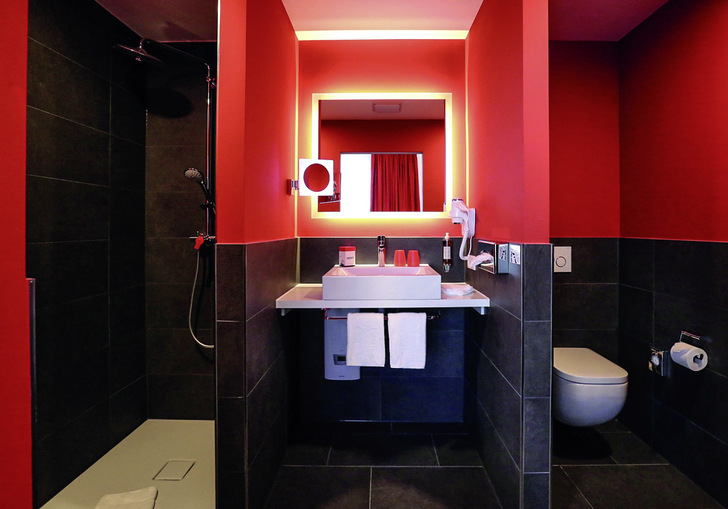 Rote Wände und schwarze Fliesen treffen in den ­Bädern des ­Domero-Hotels auf die Waschtische und Duschflächen der Serie Kaldewei Cono in Alpinweiß. - © Bild: Domero Hotel AG
