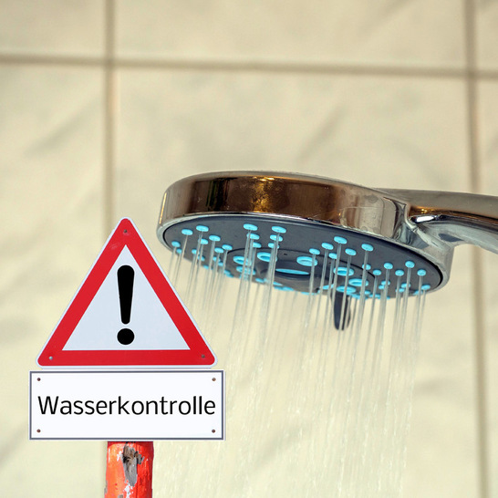 „Nahaufnahme eines modernen Duschkopfs mit Wasserstrahl; darunter ein Warnschild, auf dem in deutscher Sprache 'Wasserkontrolle' steht. Das Bild veranschaulicht die Bedeutung von technischen Lösungen zur effizienten Trinkwasserhygiene und Estriktion im Einsatzbereich der Sanitärtechnik.“. - © Getty Images/iStockphoto/Animaflora