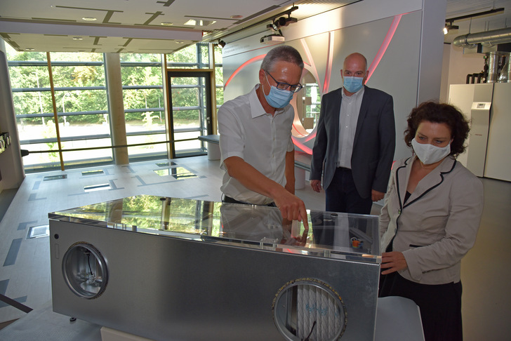 Geschäftsführer Dr. Kai Schiefelbein (links) mit Ministerin Dr. Carola Reimann am Lüftungsgerät, das speziell für den Einsatz in Klassenzimmern entwickelt wurde. Im Hintergrund Burkhard Max, Geschäftsführer der Stiebel Eltron-Tochtergesellschaft Tecalor, die das Gerät vertreibt.