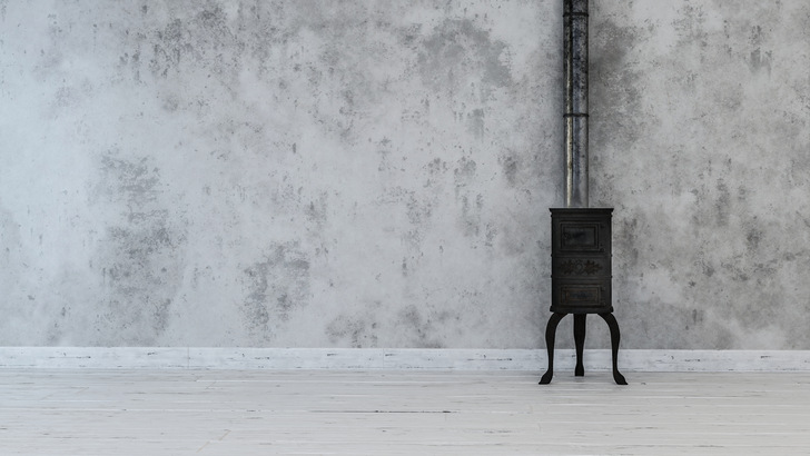Antique cast iron stove on top of white flooring with vertical metal pipe attached to dirty white wall
