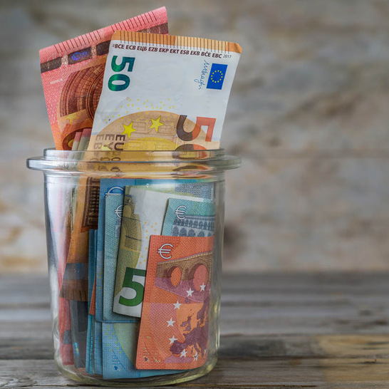 Euro bills in a glass jar on a table. Concept for saving money. Wooden background. - © Getty Images/iStockphoto/Jens Domschky
