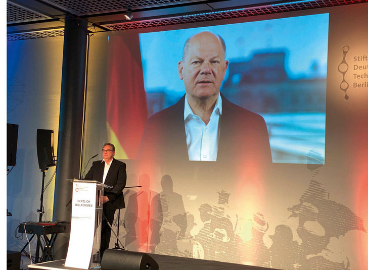 Bundeskanzler Olaf Scholz richtet ein Grußwort an die Gäste. Links: Oliver Kalkofe. Der Komiker, Kabarettist und Satiriker führte durch den Abend mit spitzen, satirischen Worten.