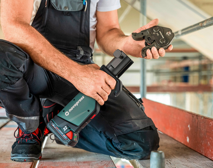 Neuer Alt-Text: „Ein SHK-Facharbeiter montiert auf einer Baustelle mit einer Novopress-Pressmaschine und Pressfitting ein Metallrohr für die Heizungs- oder Trinkwasserinstallation.“ Begründung: Der neue Alt-Text benennt präzise den Kontext (SHK-Facharbeiter, Baustelle), das Werkzeug (Novopress-Pressmaschine), die Handlung (Metallrohrmontage/Pressen) und den technischen Anwendungsbereich (Heizungs- oder Trinkwasserinstallation). Damit wird er sowohl fachlich korrekt als auch zielgruppengerecht formuliert. - © Bild: Novopress / Timo Lutz
