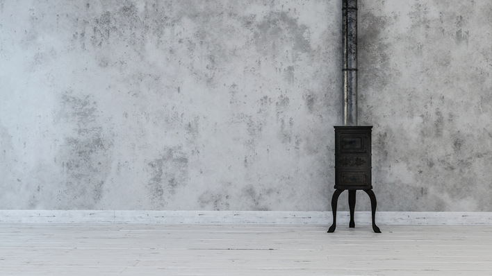 Antique cast iron stove on top of white flooring with vertical metal pipe attached to dirty white wall